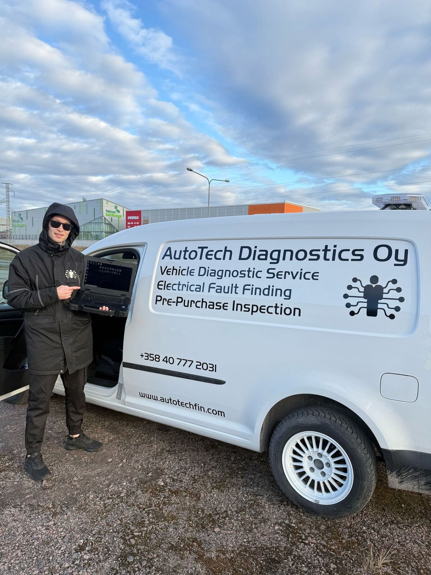 Person in a hoodie holding a laptop beside a van with AutoTech Diagnostics branding and services listed.