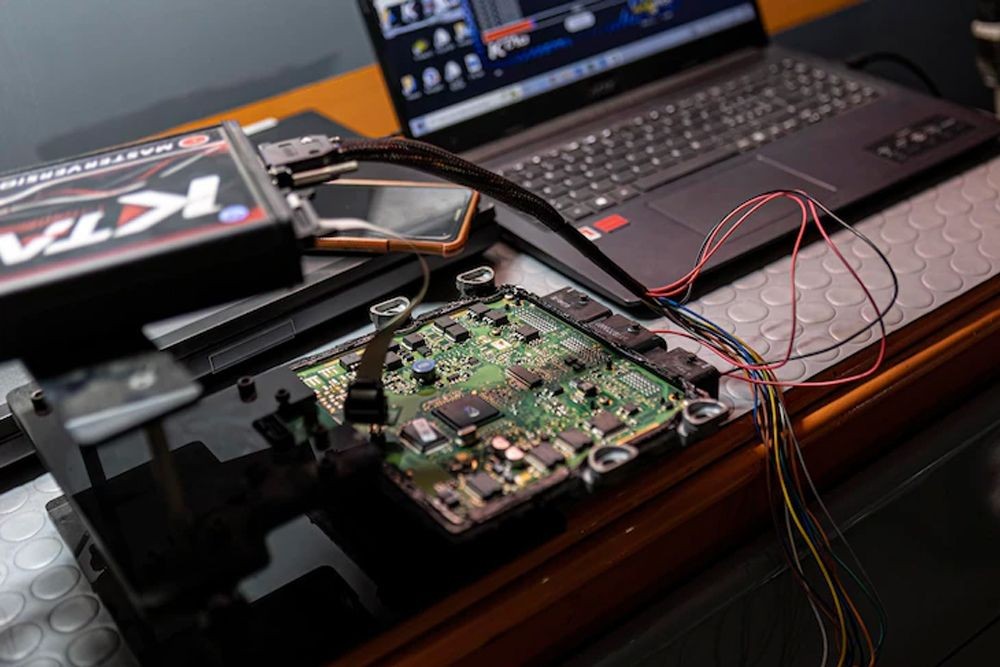A laptop connected to a circuit board via multiple colored wires, with electronic testing equipment placed nearby.
