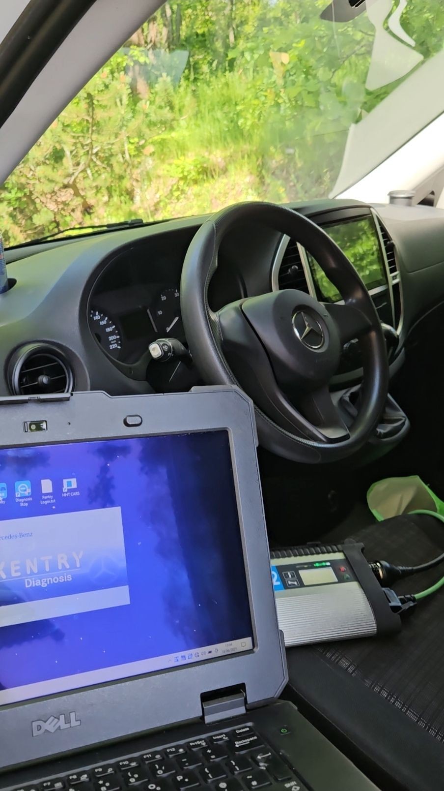 Car interior with Mercedes steering wheel and laptop running diagnostic software.